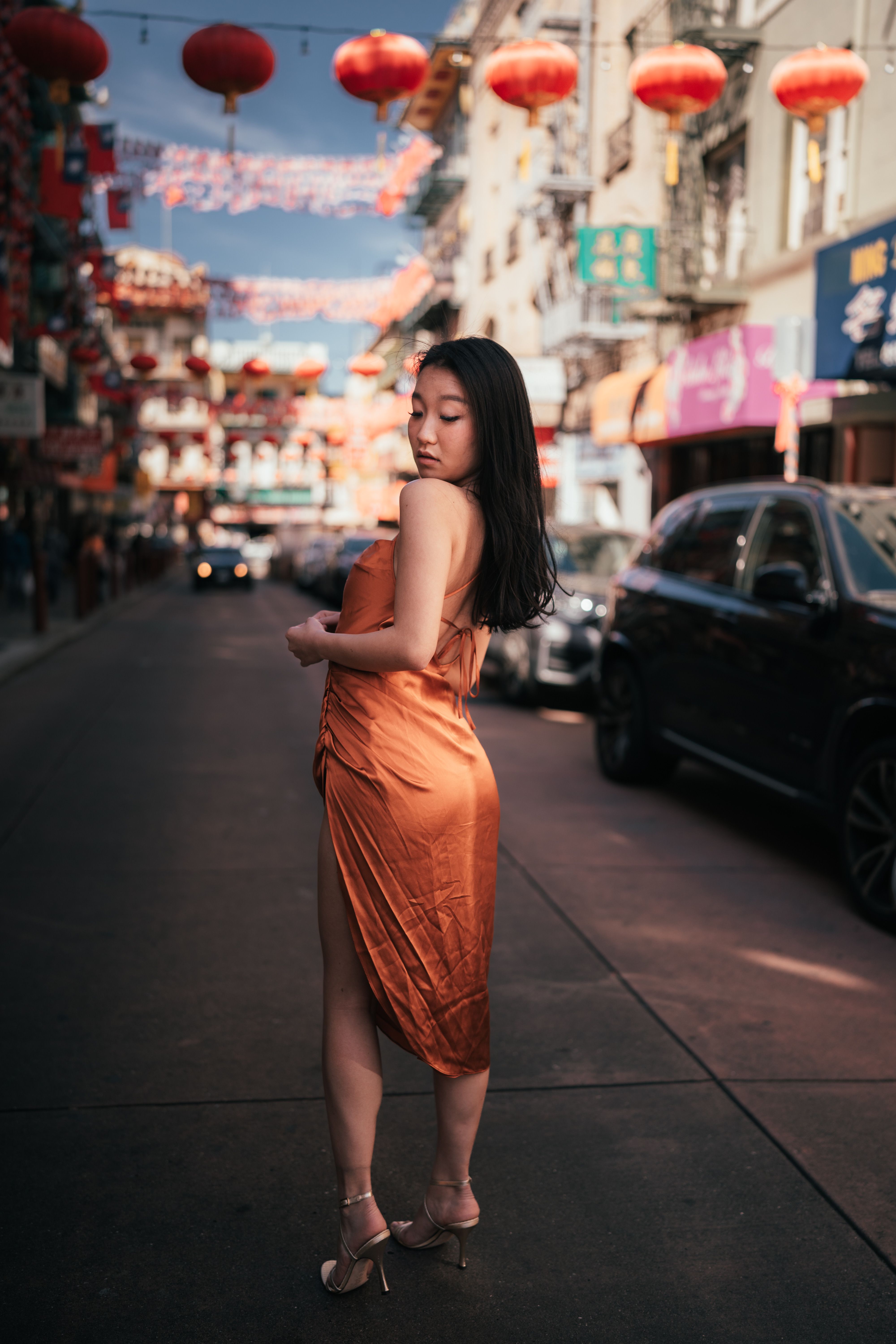 Fashionable Asian woman in a brown dress standing on a vibrant city street, exuding elegance.