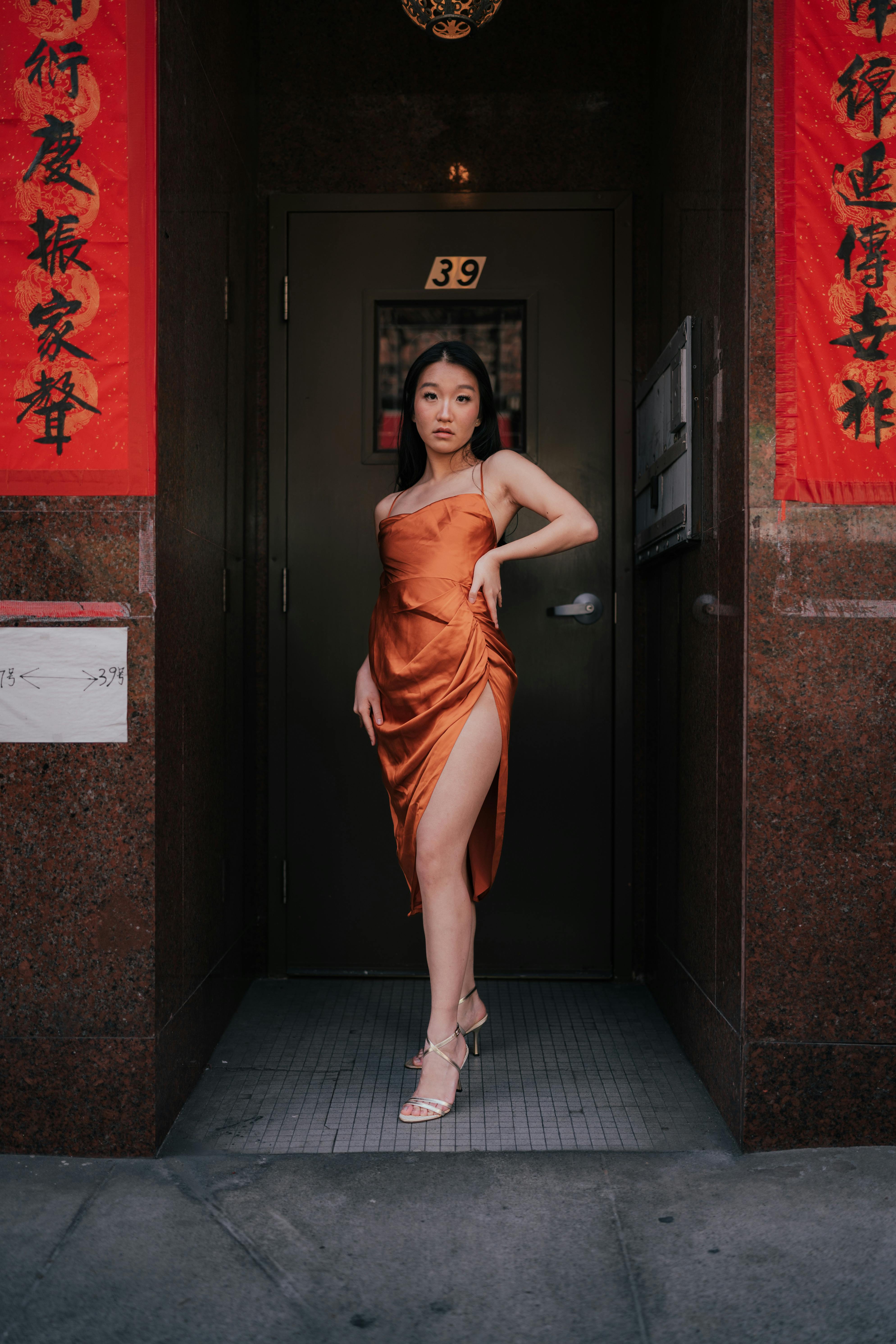 Woman in orange dress posing confidently in front of a decorated doorway.