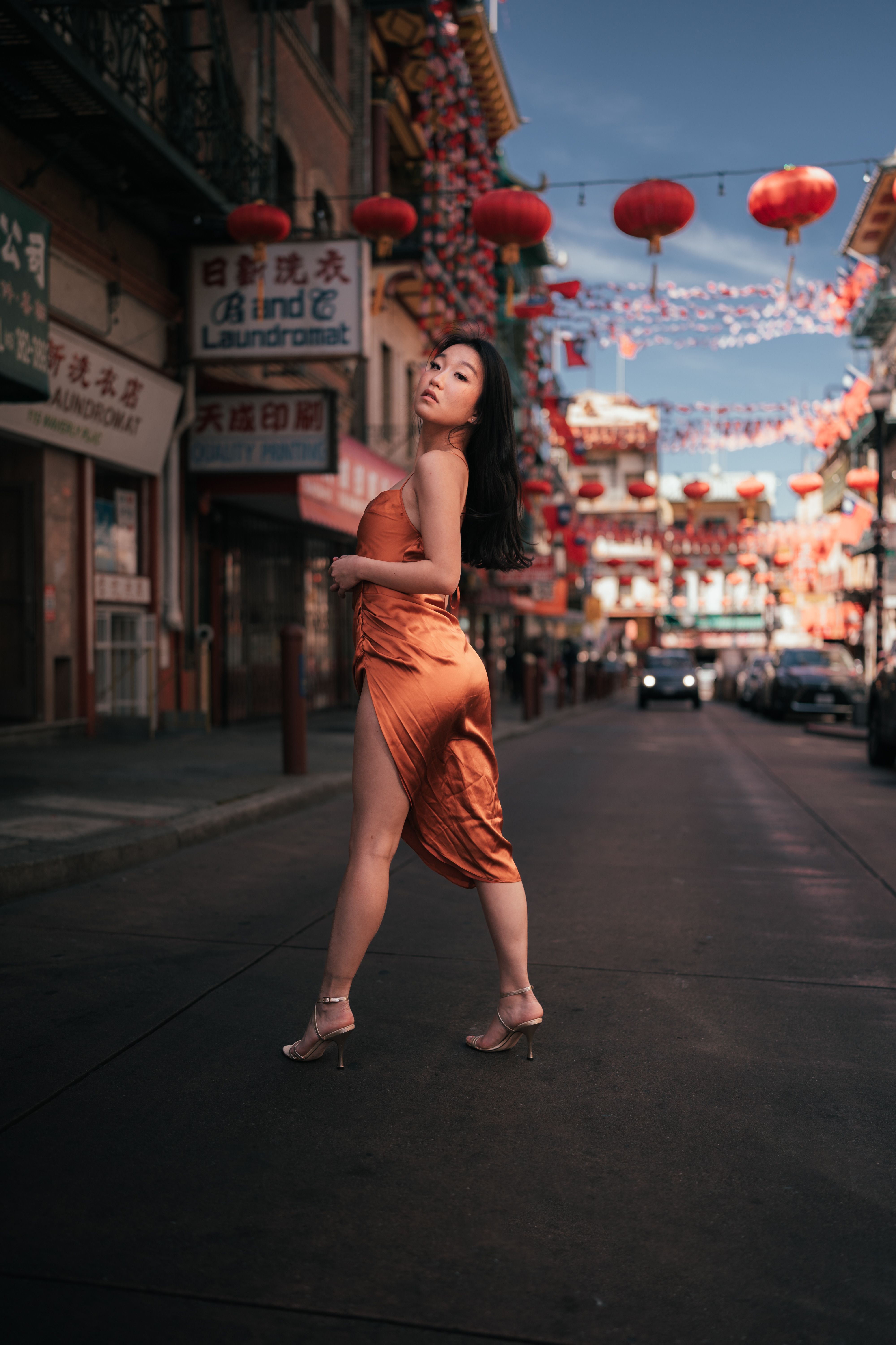 Stylish woman in silk dress poses gracefully in vibrant Chinatown, showcasing urban fashion.