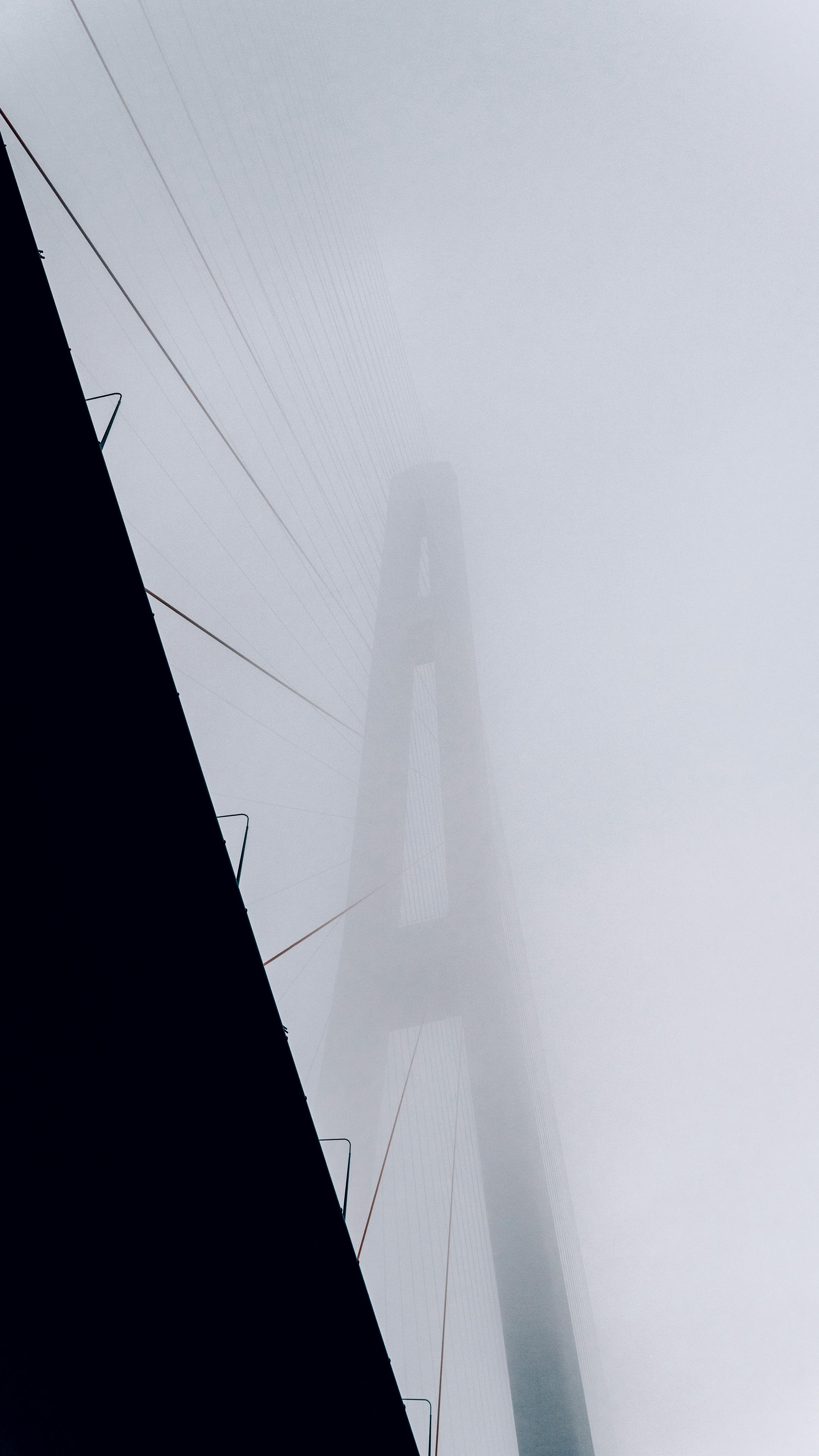 A dramatic view of a suspension bridge shrouded in dense fog, creating a mysterious atmosphere.