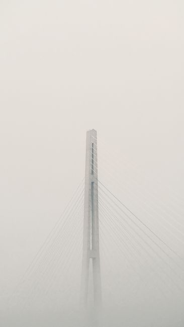 A bridge peeks through dense fog creating a minimalist and serene urban landscape.