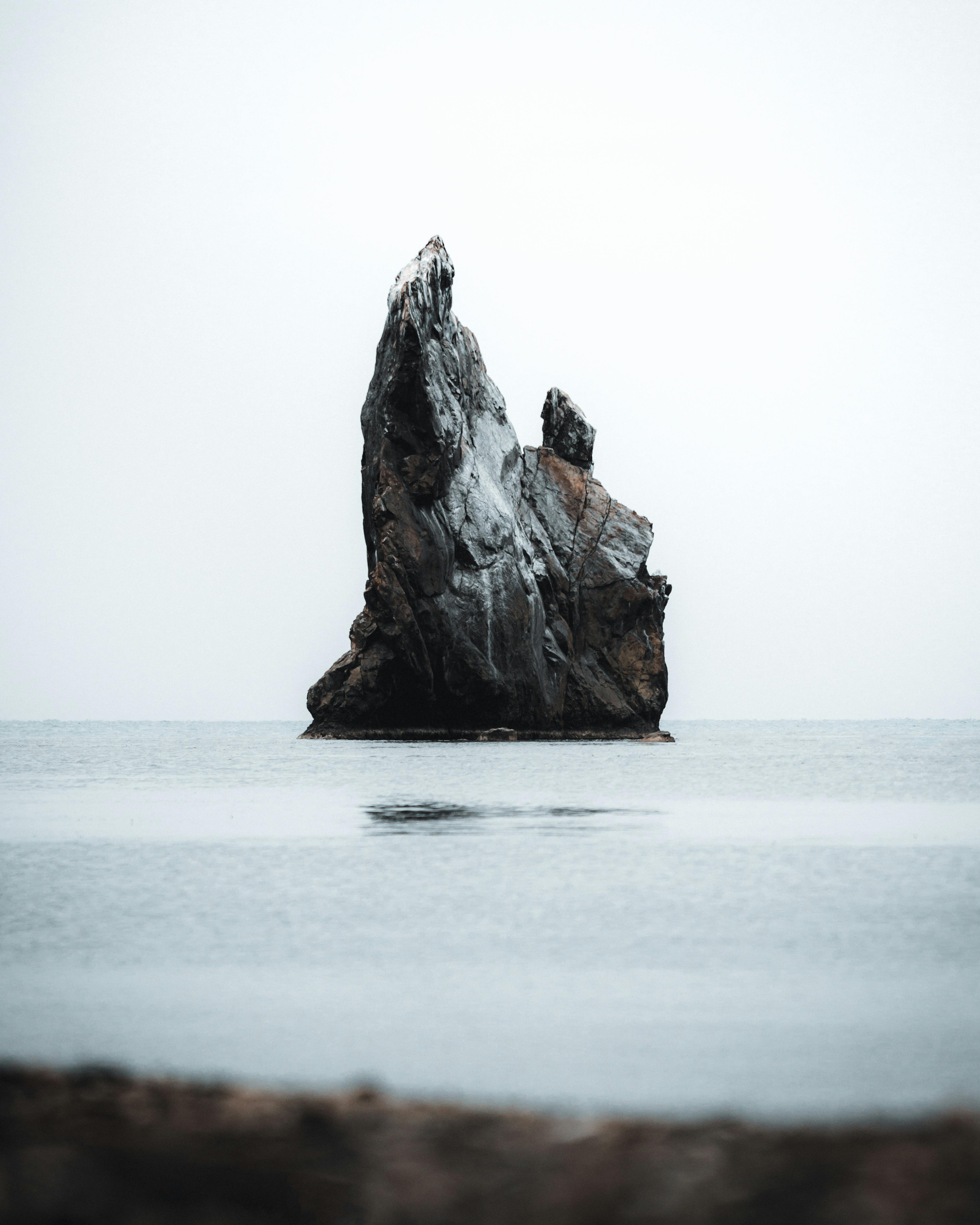 A towering rock formation emerges from calm sea waters, showcasing nature's serene beauty.
