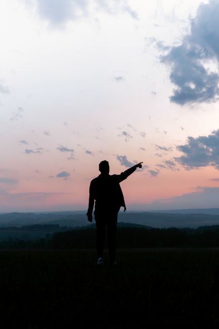 A silhouette of a man pointing into the colorful twilight sky, creating a scenic and dramatic view.
