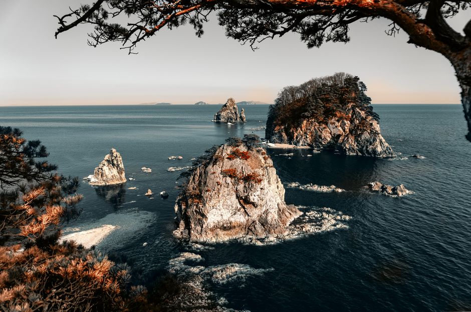 Breathtaking scene of rocky islands amidst the reflecting sea, framed by trees.