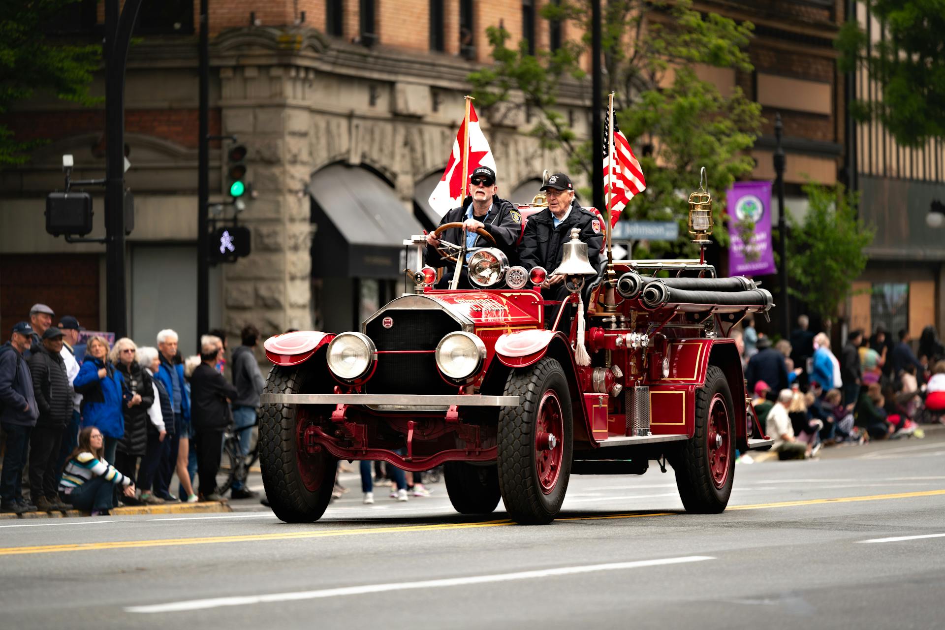 A vintage fire truck drives in a festive parade in Victoria, BC, Canada with flags displayed.