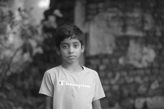 Black and white portrait of a young boy standing outdoors with a pensive expression.