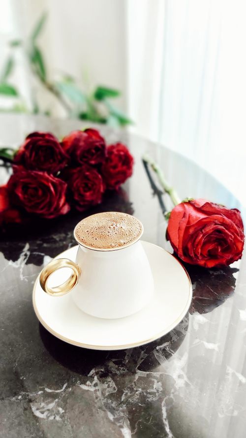 Free A cup of frothy coffee and vibrant red roses on a black marble table setting. Stock Photo