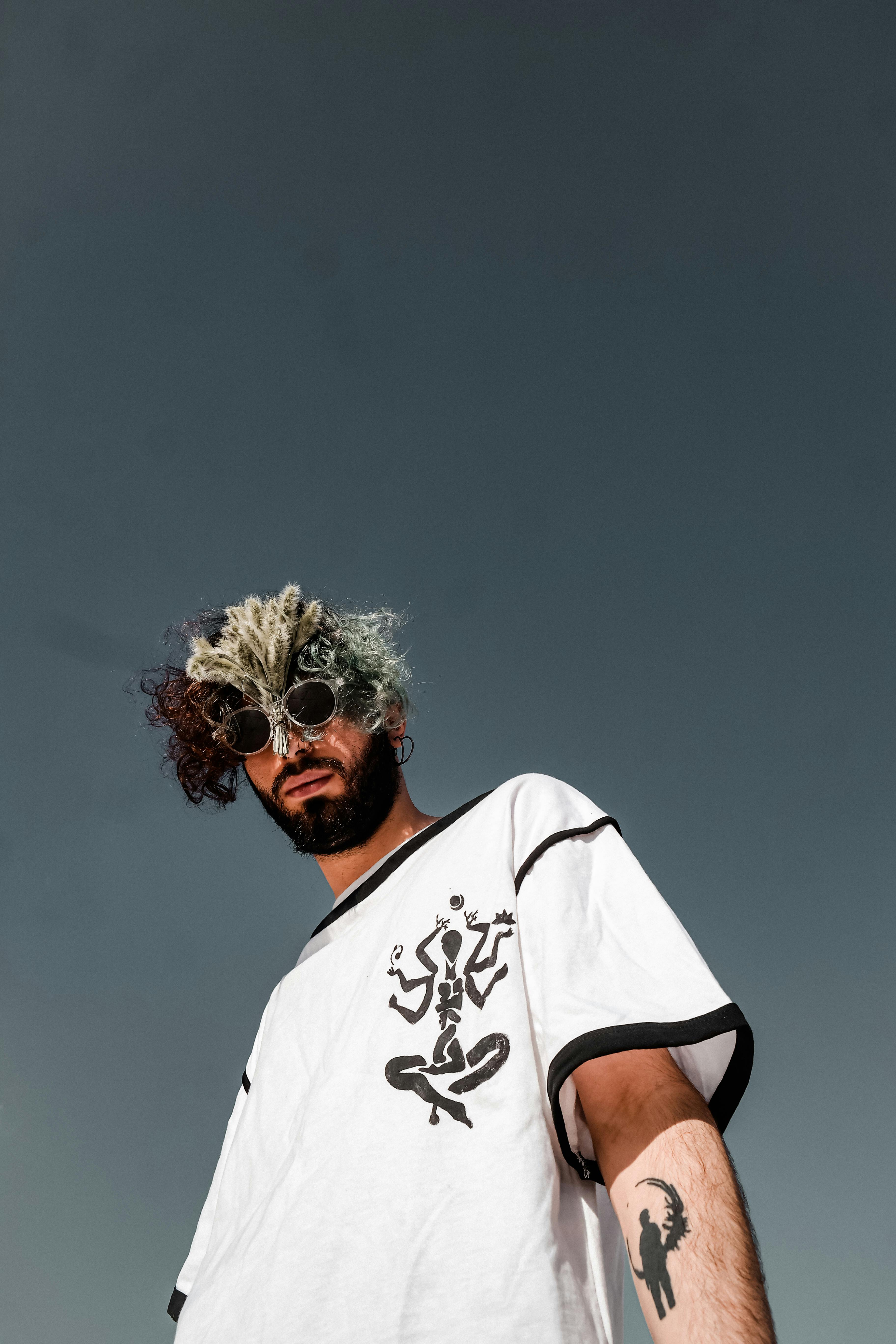 Stylish man with multicolored hair and sunglasses wearing a printed t-shirt outdoors.