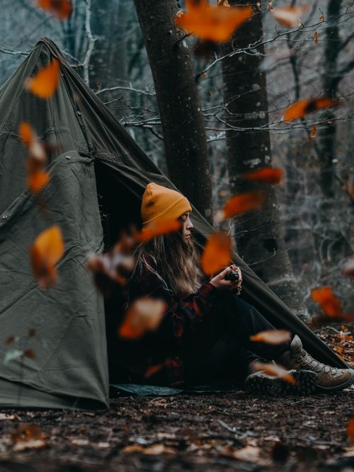 Free Woman sitting by a tent in a forest during autumn with leaves falling around. Stock Photo