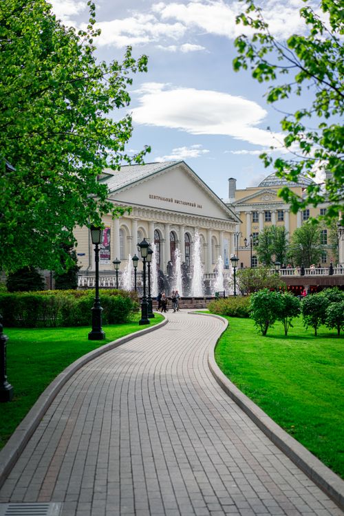 Free Pathway in a lush urban park leading to a historic building with fountains. Stock Photo