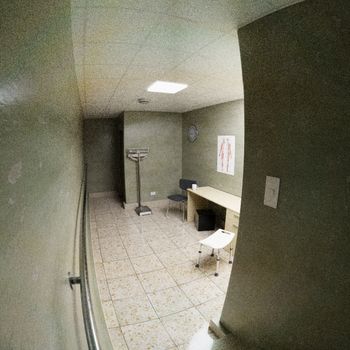 A simple empty medical examination room with desk, chairs, and medical equipment.