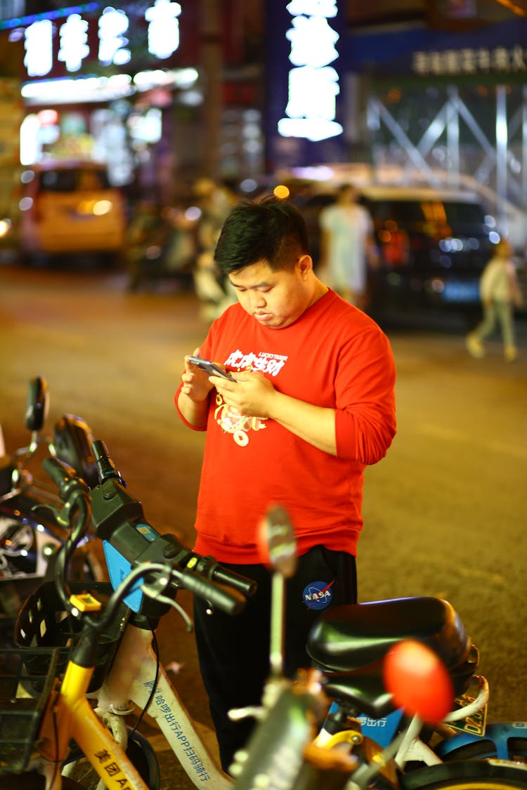 Man Using Phone Standing In Front Of Rows Of Bicycles