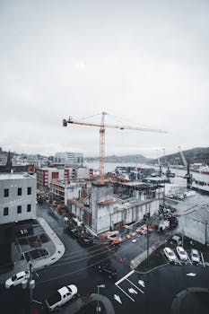 Aerial view of a city construction site featuring a prominent tower crane and surrounding buildings.