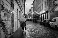 Black and white street scene in Lviv, featuring a person with an umbrella on a cobblestone road.