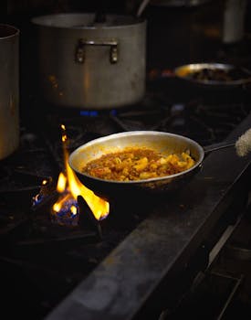 A chef skillfully prepares a pasta dish over an open flame in a professional kitchen.