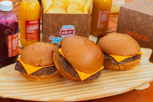 Three cheeseburgers with drinks and snacks on a wooden platter, perfect for casual dining.