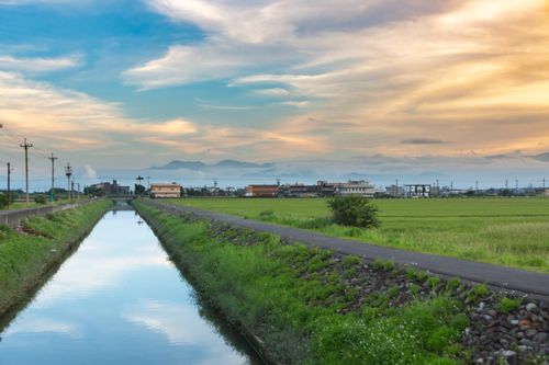 Free Captivating farmland landscape with a tranquil canal under a vibrant sunset sky. Stock Photo