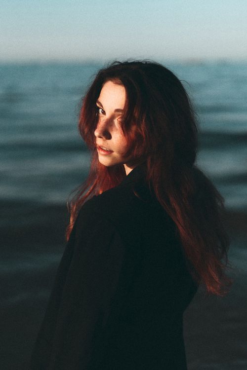 Free Portrait of a woman with long hair by the ocean during twilight, with a moody atmosphere. Stock Photo
