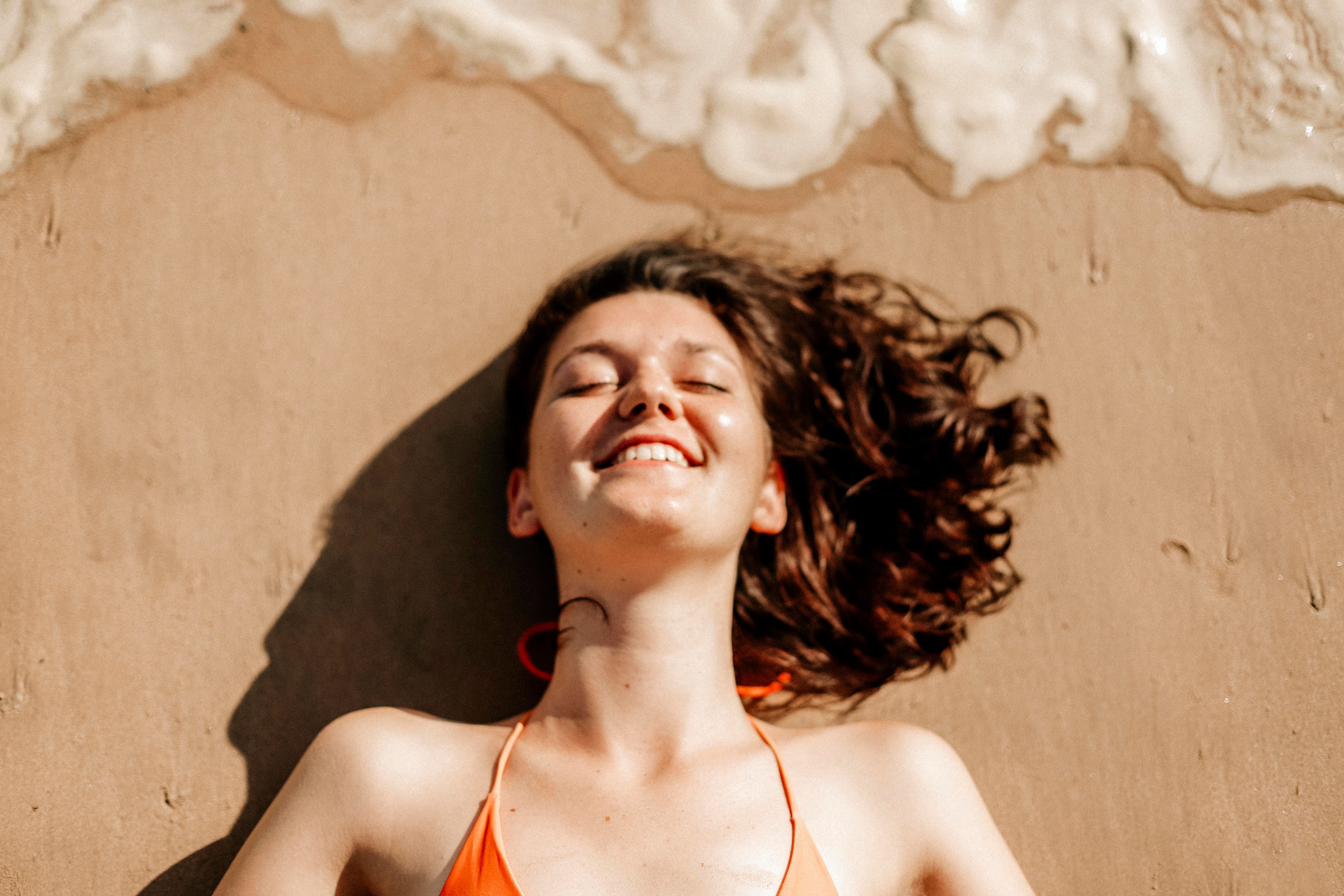 A smiling woman relaxes on Weligama beach, Sri Lanka, with waves gently breaking near her.