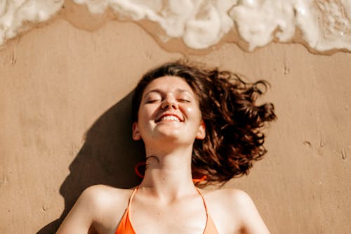 Free Woman in Orange Tank Top Lying on Brown Sand Stock Photo