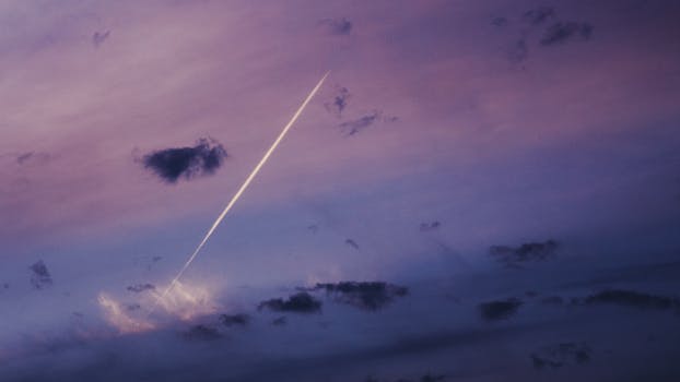 Beautiful sunset with vibrant pink and purple hues, featuring a dramatic contrail across the sky.