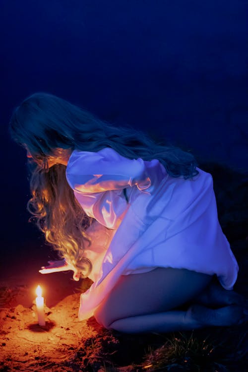 Side View of a Person Kneeling beside a Lighted Candle