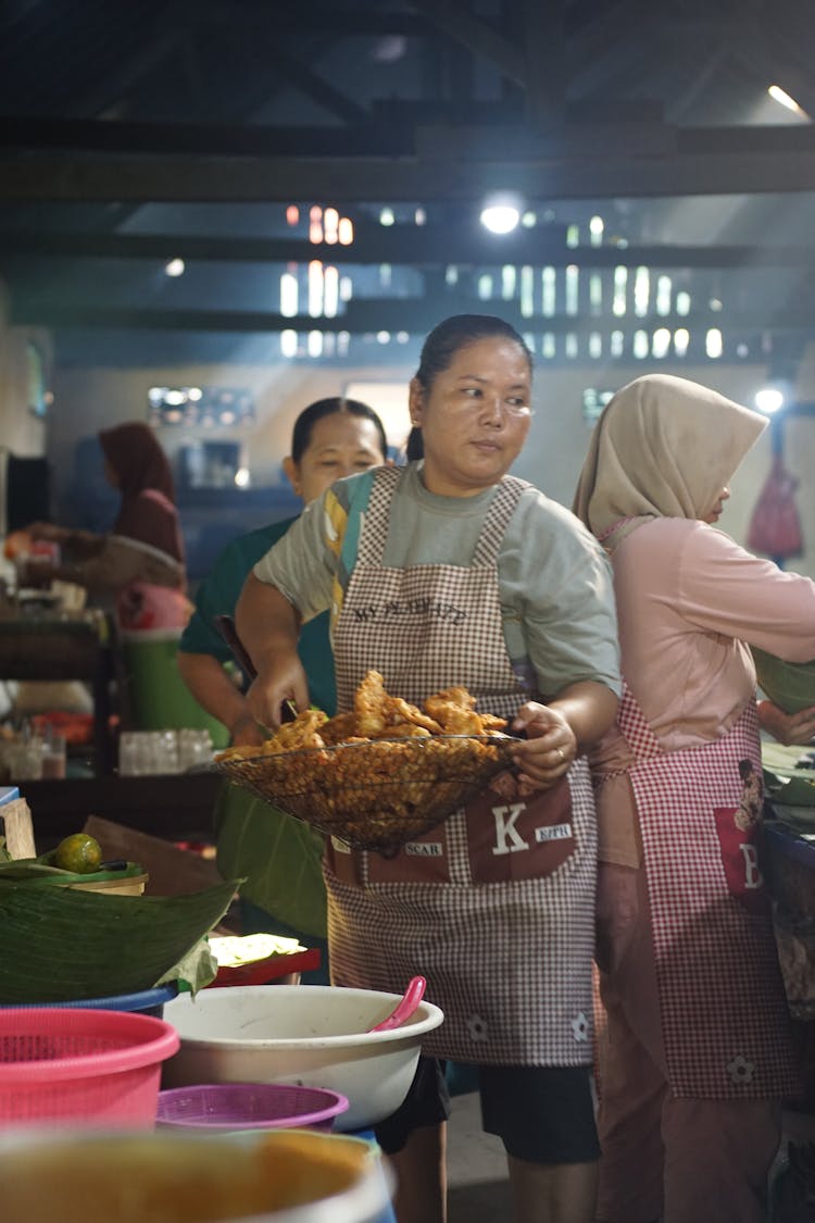 A Woman Wearing Apron Holding A Strainer With A Bunch Of Fried Food