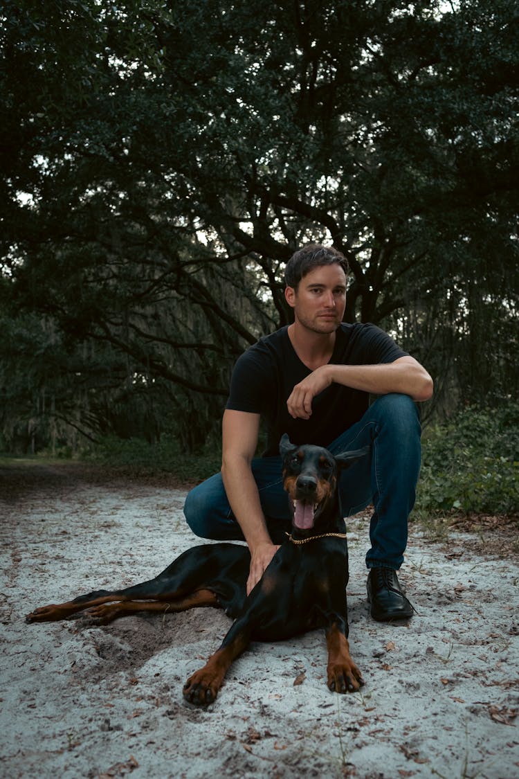 Man Kneeling On Sand Next To Dog