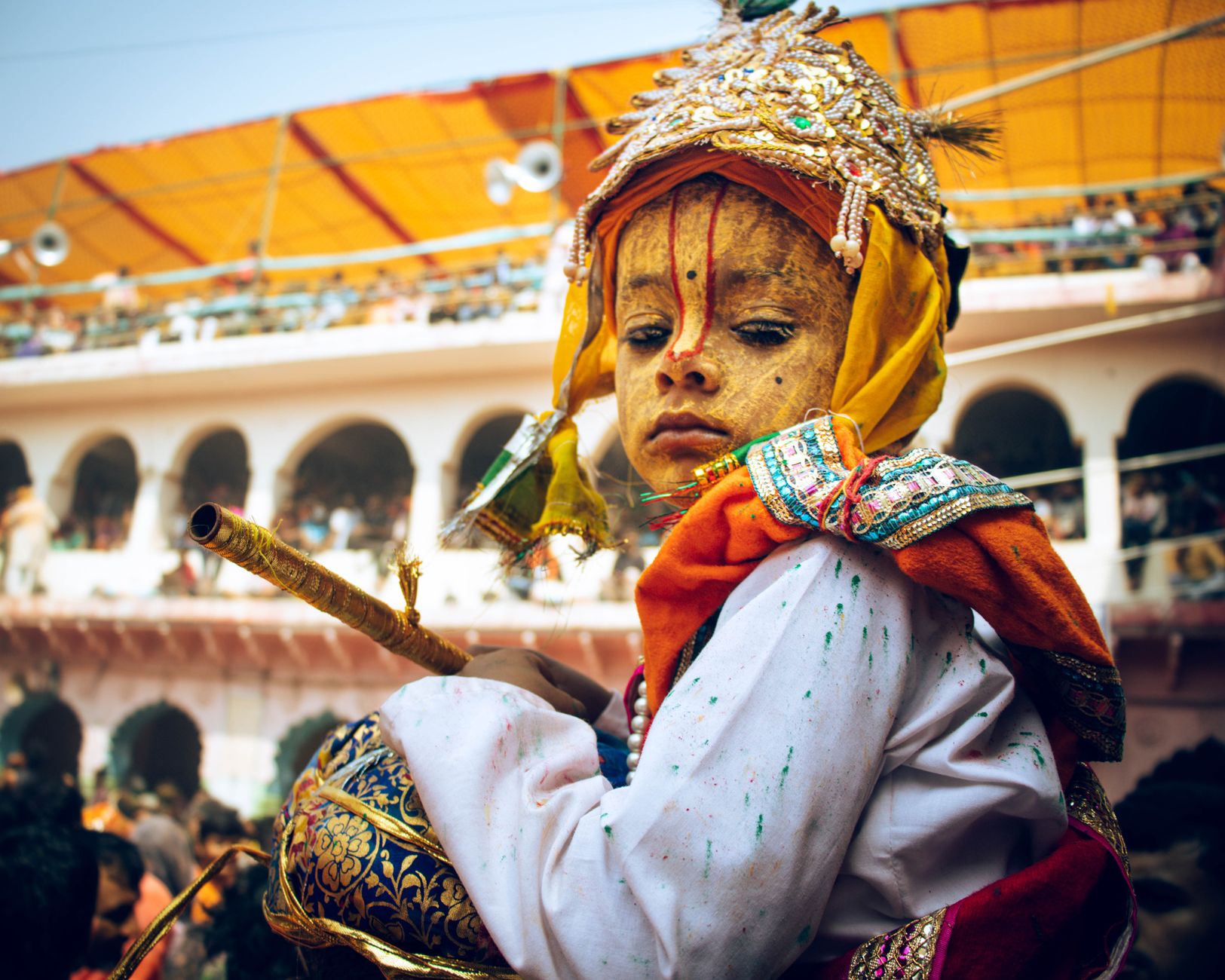 A child dressed in vibrant traditional attire participates in a colorful Indian festival, celebrating cultural heritage.