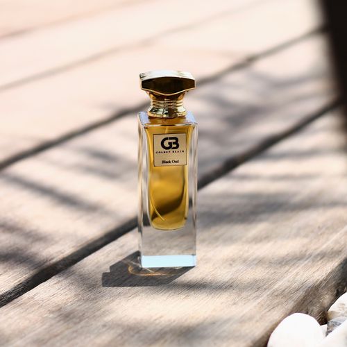 Free Close-up of a luxurious golden perfume bottle casting a shadow on a wooden surface. Stock Photo