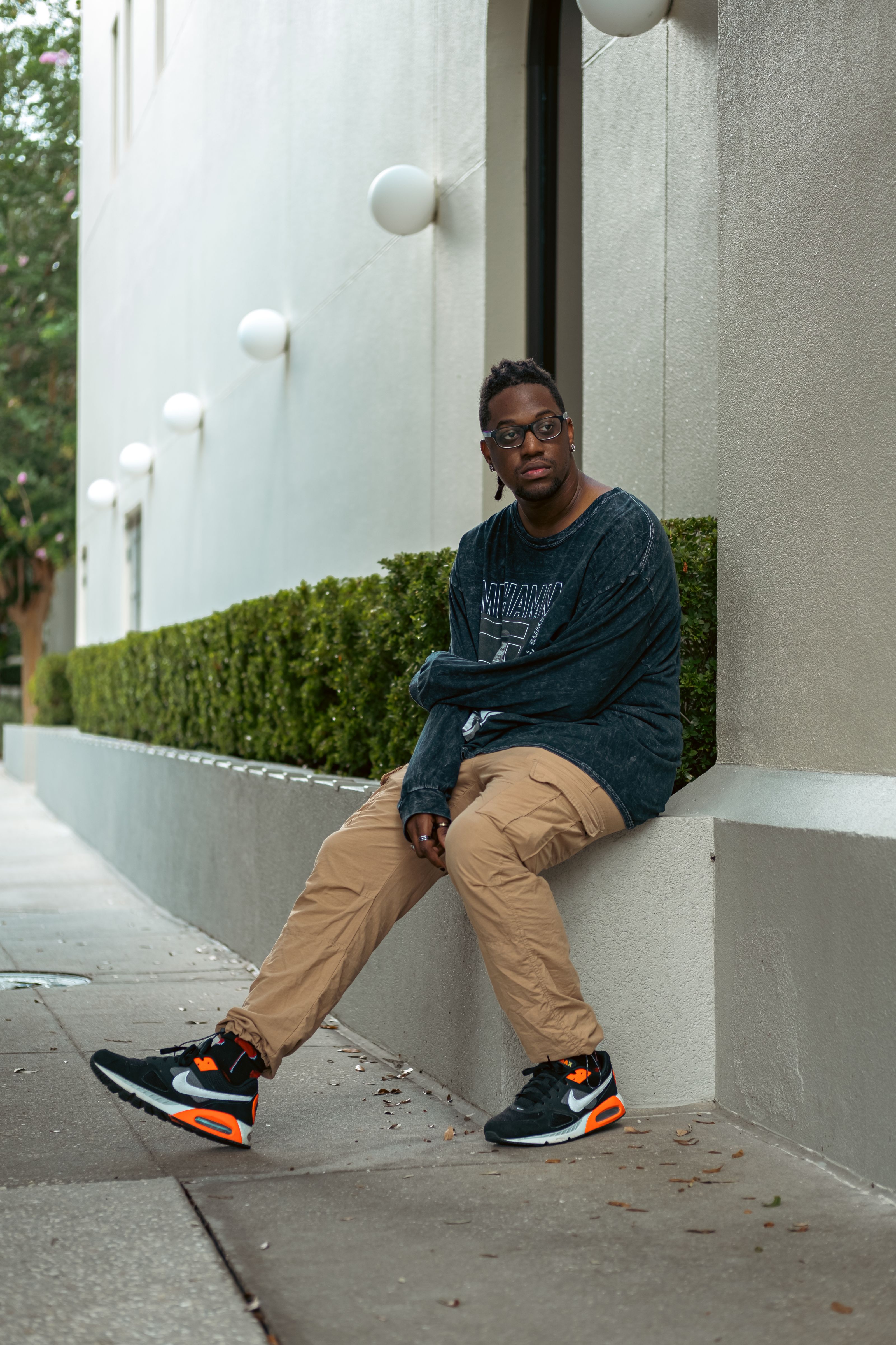 Um homem fashionista senta-se em uma beirada com roupas de rua modernas, exalando estilo e confiança.