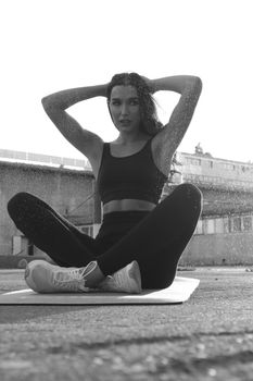 A woman sitting outdoors in a yoga pose wearing black activewear in a monochrome setting.