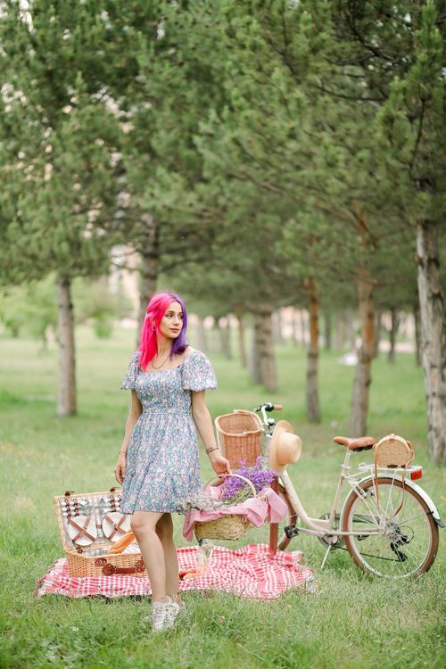 Free Colorful scene with a woman by a picnic setup in a lush park with trees and bicycle. Stock Photo