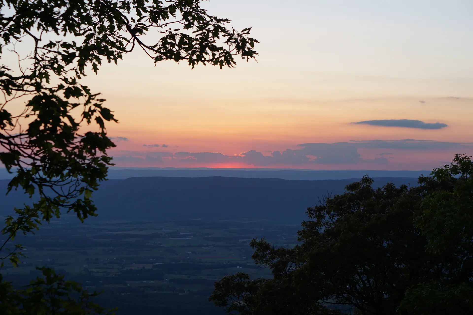 A peaceful sunset view over rolling hills and valleys, framed by trees. A peaceful sunset view over rolling hills and valleys, framed by trees.