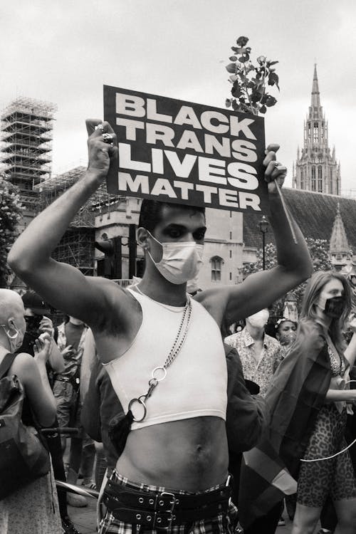 A Grayscale Photo of a Man Wearing Face Mask while Holding a Placard