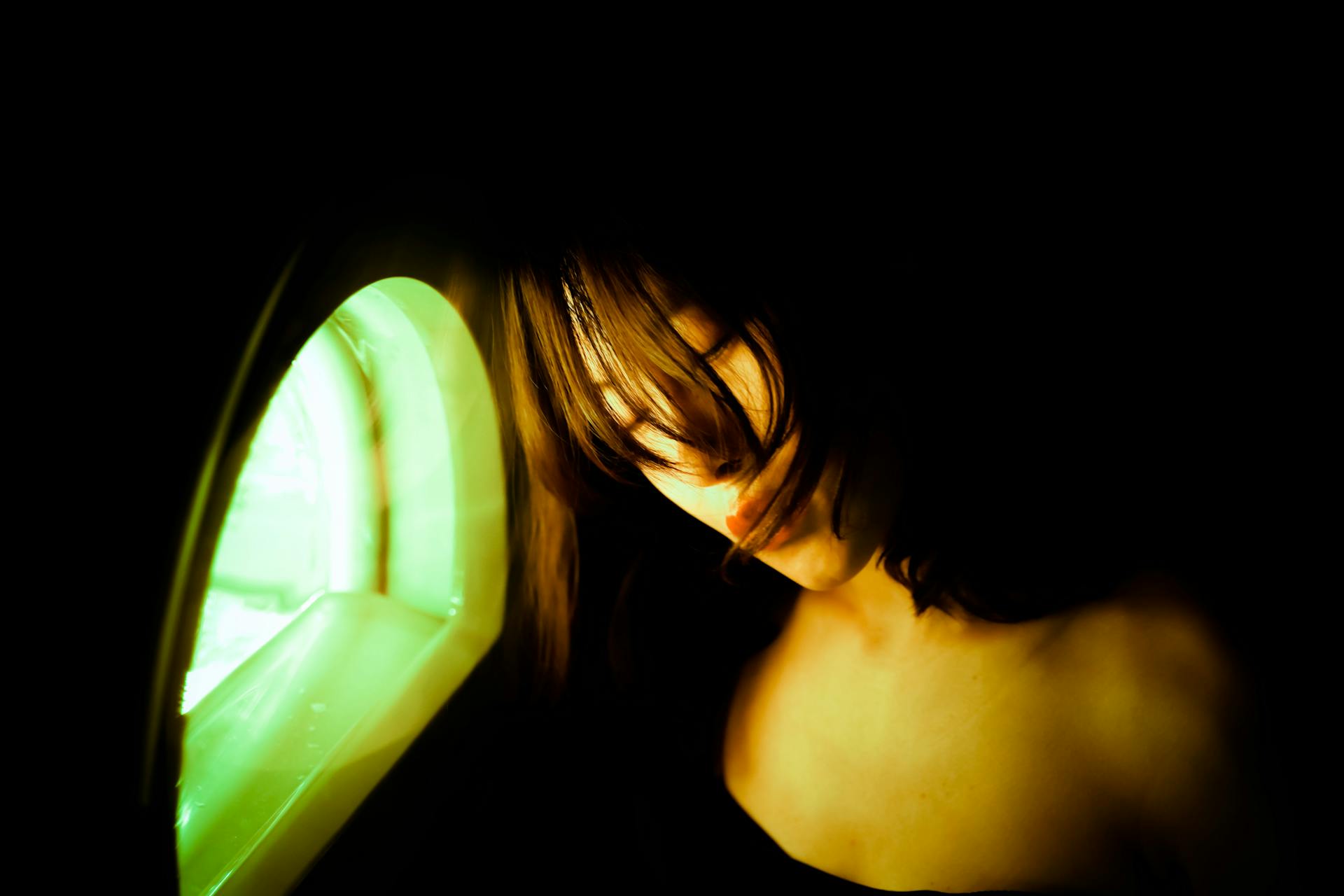 A woman illuminated by green light from a small window, creating a moody ambiance.