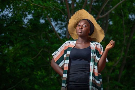 Graceful portrait of a woman in a striped outfit and straw hat against a lush green background.