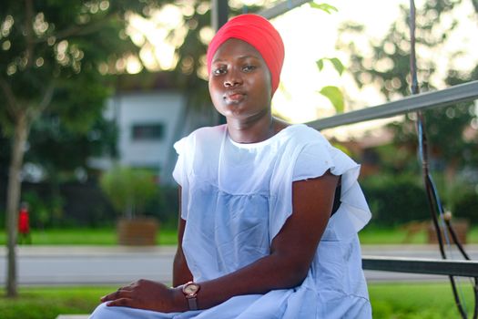 Portrait of a woman in a red headscarf sitting in a park in Abidjan, Côte d'Ivoire.