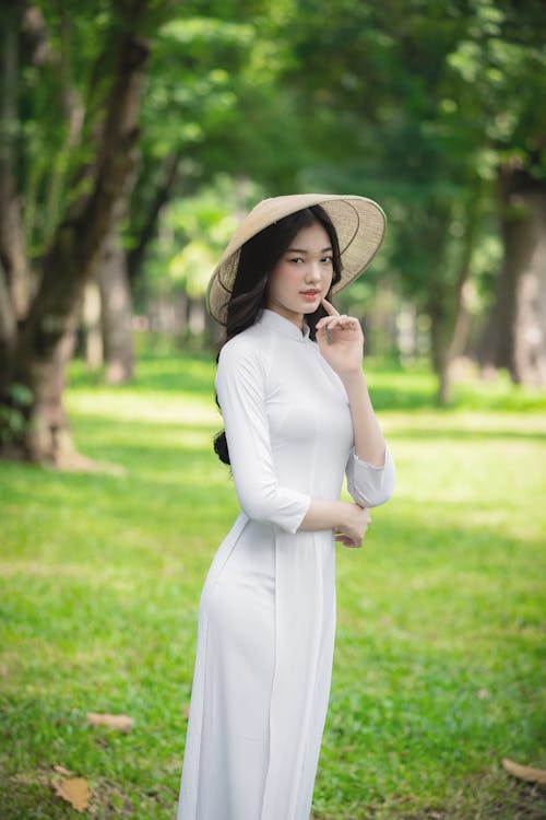 Woman in White Long Sleeve Dress Wearing Brown Sun Hat Standing on Grass Field