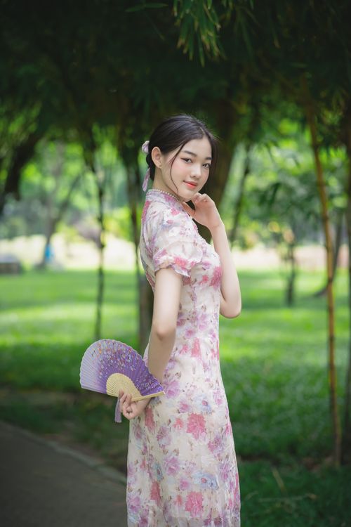 Free Portrait of an Asian woman in a floral dress holding a fan outdoors in a serene park. Stock Photo