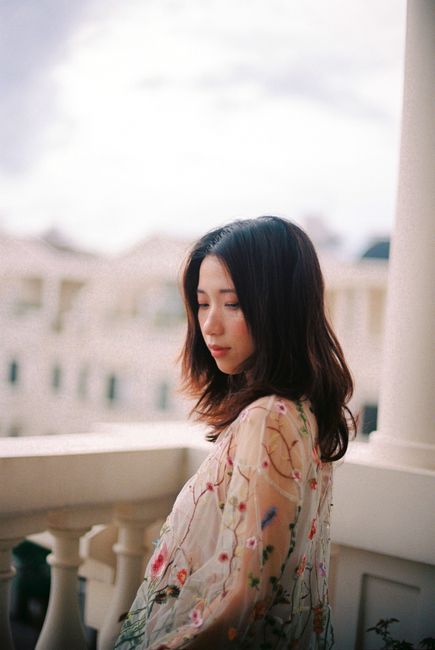 A serene portrait of an elegant Asian woman standing on a balcony, captured with soft natural lighting.