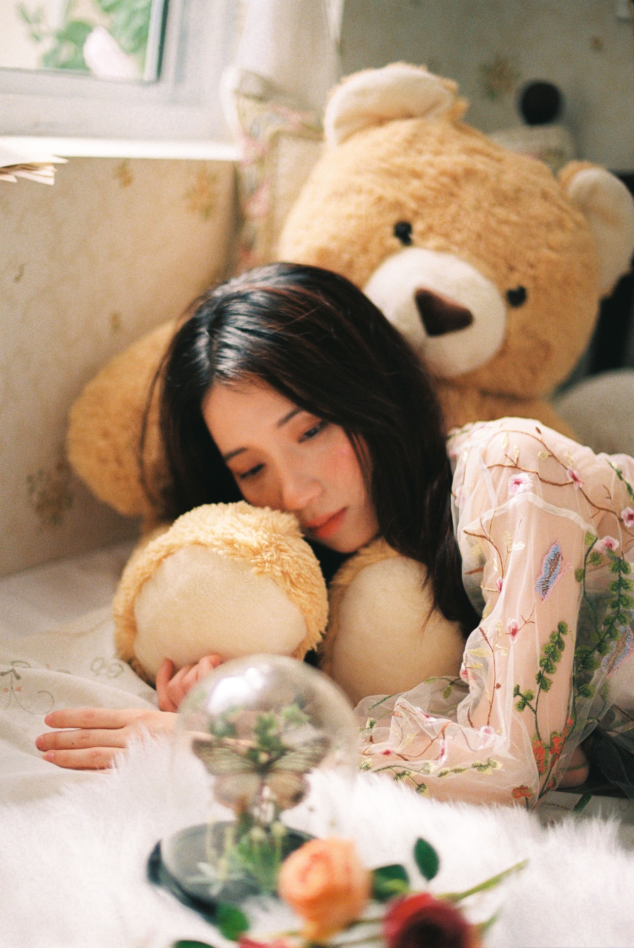 A serene scene of an Asian woman lying on a bed with stuffed teddy bears indoors.