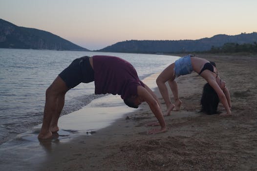 A couple performing yoga poses on Methoni Beach at sunset, showcasing fitness and tranquility.