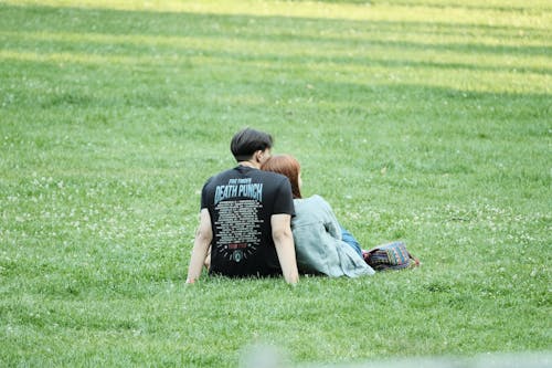 Man in Black Shirt Sitting on Grass Field Beside Woman in Blue Denim Jacket