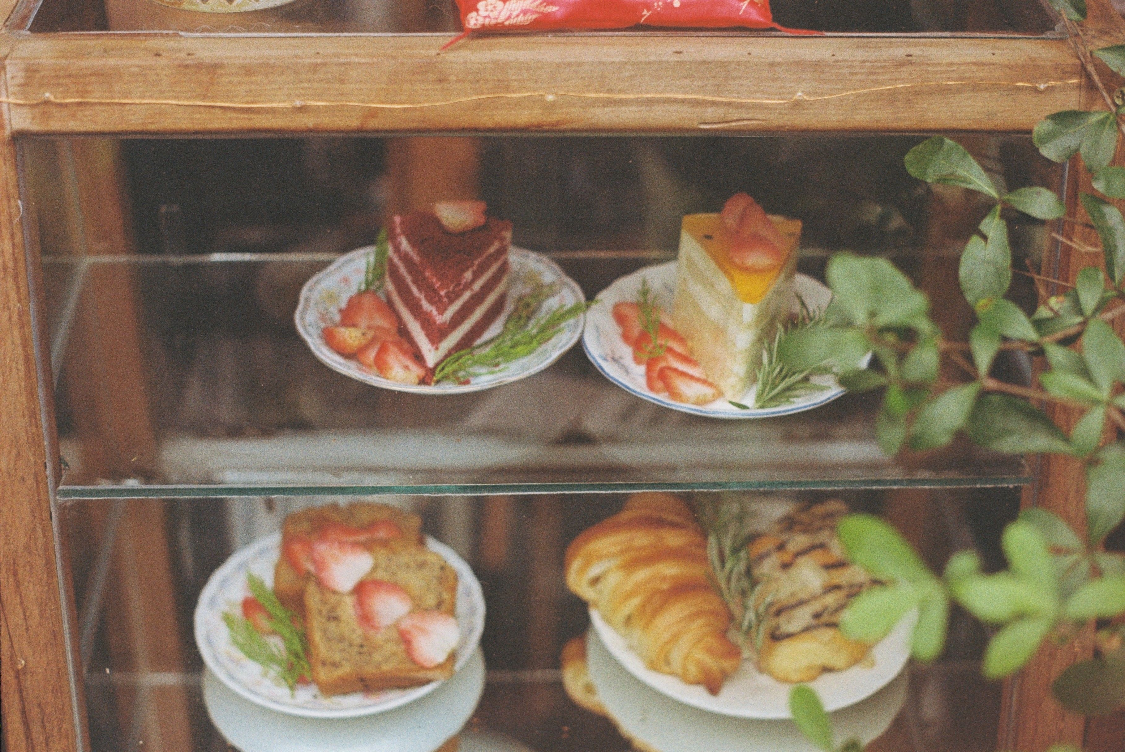 A showcase of delectable cakes and pastries adorned with strawberries, captured invitingly in a glass cabinet.