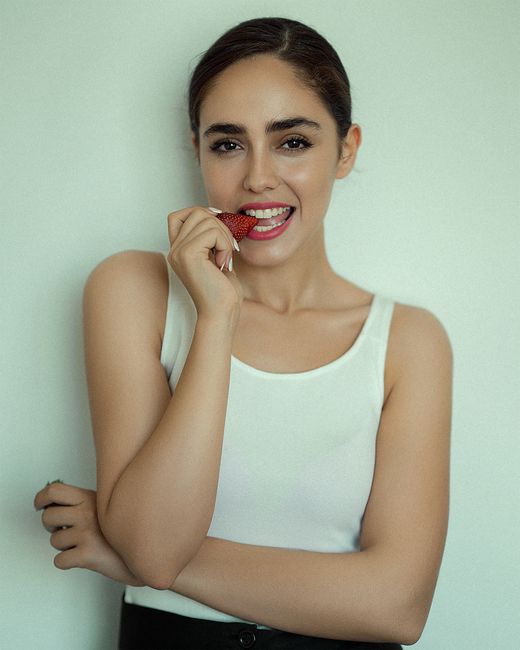 Portrait of a smiling woman enjoying a strawberry against a plain background.