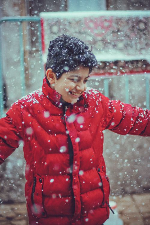 Free A happy child in a red puffer jacket enjoying snowfall outdoors. Winter fun captured. Stock Photo