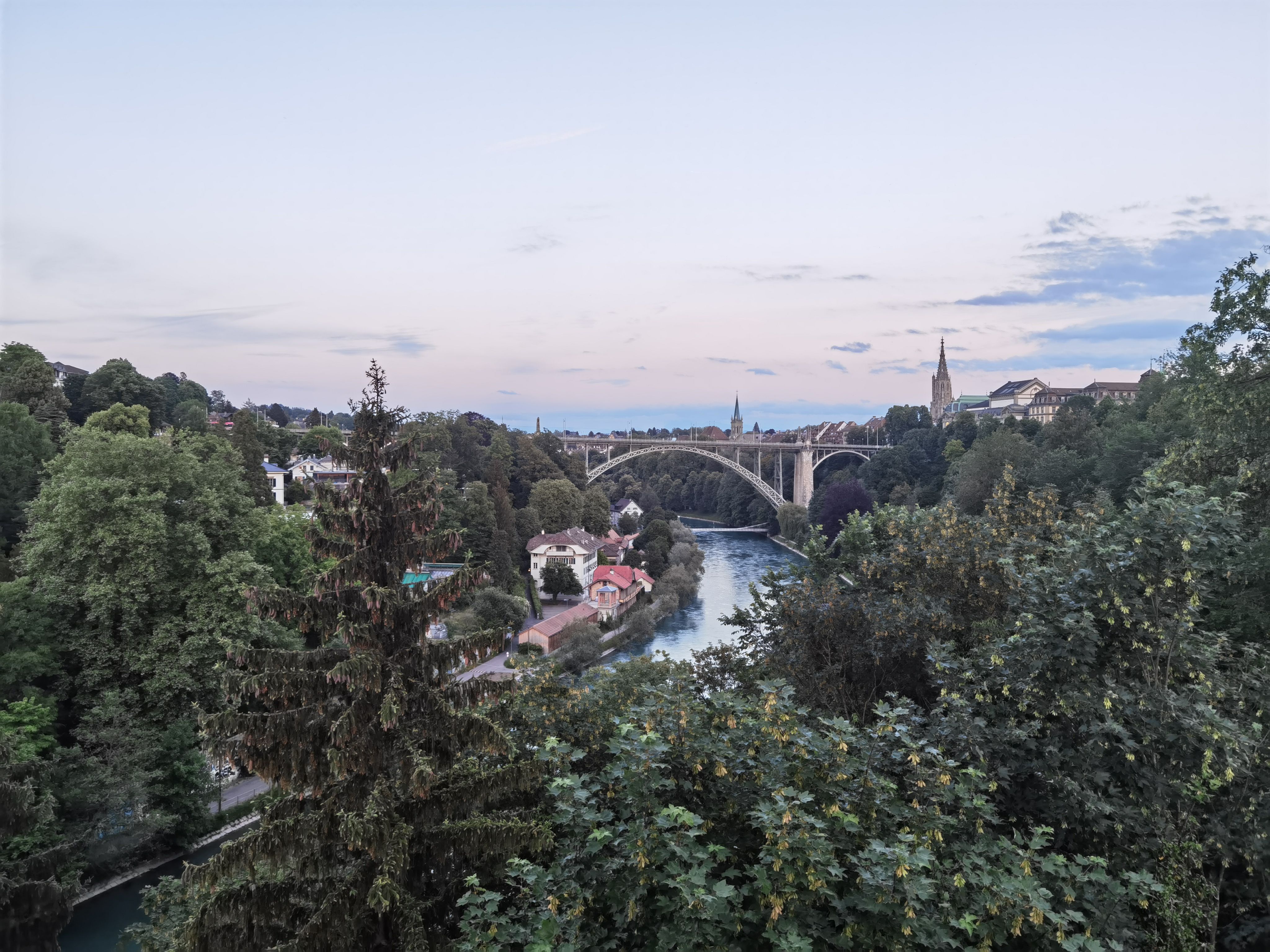 A picturesque view of Kornhausbrücke with lush greenery and river in Bern, Switzerland during dusk.