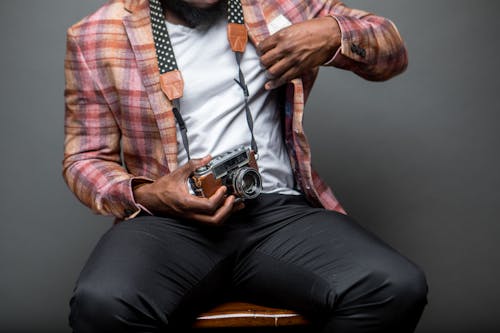 Man Wearing Button-up Shirt Holding Black and Brown Camera While Sitting on Chair