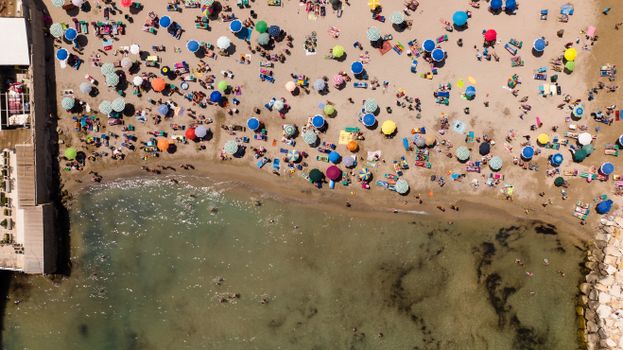 Colorful aerial view of a crowded beach with umbrellas and people on a sunny day.